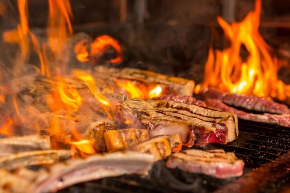 costillas asadas sobre parrilla con llamas intensas de fuego y humo en barbacoa tradicional